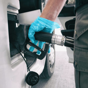 Coronavirus gas oil prices dropping man pumping gasoline at gas station wearing medical blue glove as COVID 19 spreading safety protection for touching germs