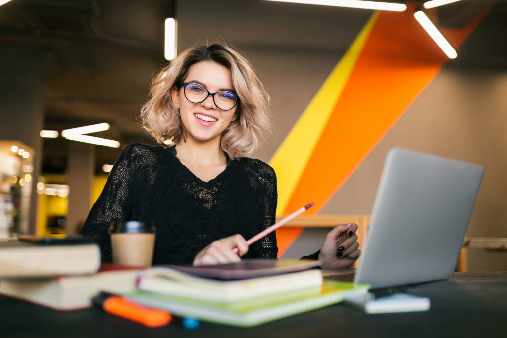 retrato de joven mujer bonita sentada la mesa con camisa negra trabajando en un portatil en la oficina de trabajo conjunto con gafas